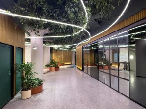 Modern offentlig miljö med brandsäkra konstväxter i krukor och hängande grönska i taket, integrerad belysning och skandinavisk design i kontorsmiljö.