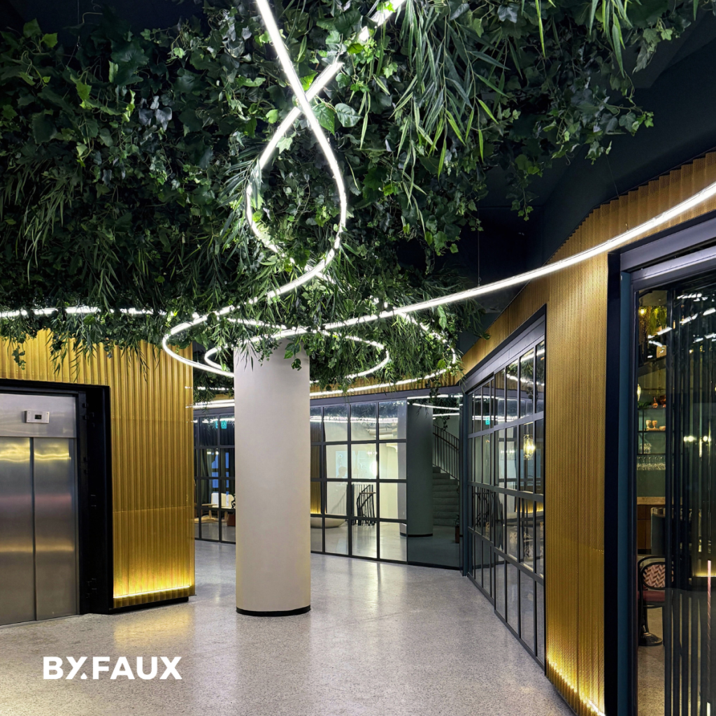 Hängande installation med brandsäkra konstväxter och integrerad belysning i modern offentlig miljö med skandinavisk design.