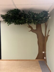 Målat träd på vägg kombinerat med hängande konstväxter i tak i skolmiljö