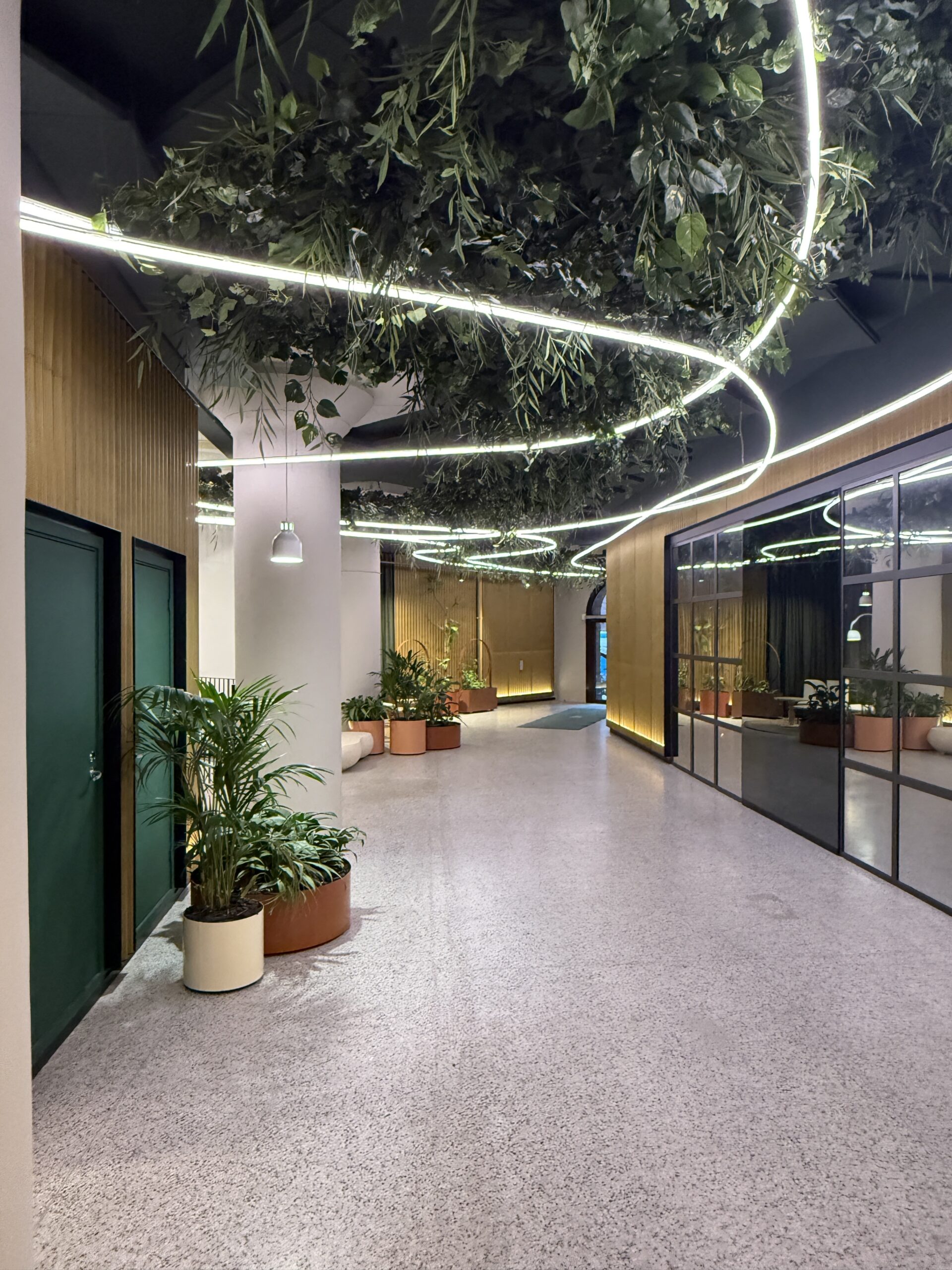 Hängande installation med brandsäkra konstväxter och integrerad belysning i modern offentlig miljö med skandinavisk design.